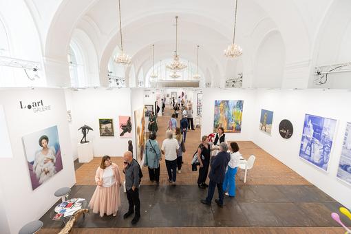Das Foto zeigt eine Ausstellungsansicht der Kunstmesse Art Vienna in der Orangerie des Schlosses Schönbrunn. Zu sehen sind Gemälde, Skulpturen und Publikum, das durch die Ausstellungsräume flaniert
