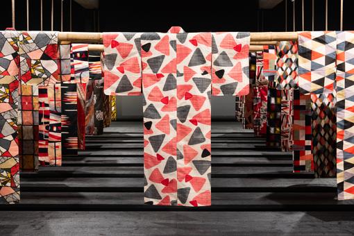 Die Ausstellungsansicht zeigt zahlreiche auf Bambusstangen hängende Meisen-Kimonos mit unterschiedlichen Mustern und Farbkombinationen