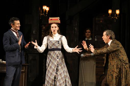 The scene photo shows the leading actress in a checked strap dress and white blouse with three books on her head, flanked by two men, one in a dark blue suit, the other in a brown paisley housecoat