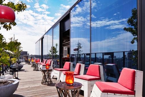 Photo of the rooftop bar The attic of the 25hours Hotel, white seating with red poufs, small cocktail tables with lanterns, plants in tubs