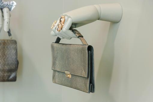 Die  Ausstellungsansicht aus der Schau "Sidekicks. Ringe und Taschen aus der MAK Sammlung" zeigt eine weiße Hand aus Kunststoff mit großen goldenen Ringen, die wie aus der Wand ragt und eine Designerhandtasche hält.