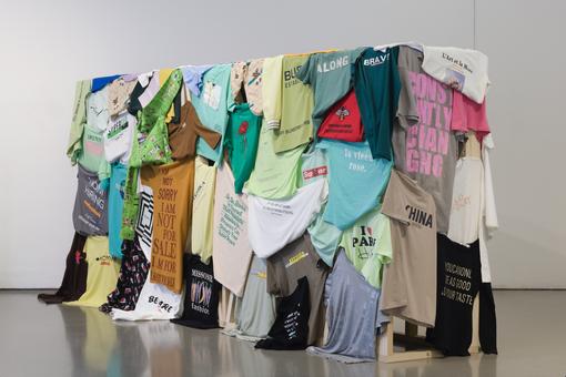 The photo shows a wall on which various colorful T-shirts with text prints, inscriptions and logos are hanging