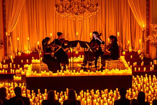 Photo of a chamber music ensemble on a pedestal surrounded by countless illuminated candles, in front of it in the darkness the audience