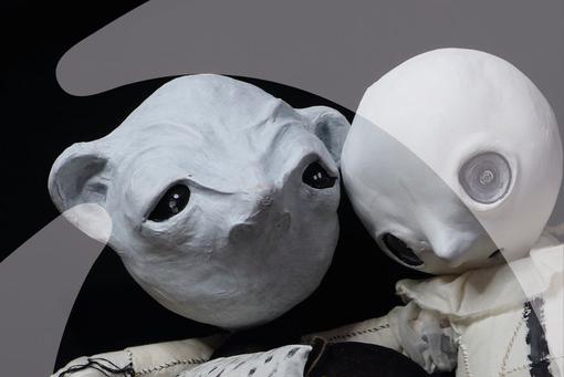 Two futuristic looking white doll heads with big sad eyes
