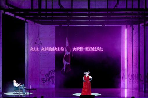 A figure in a pig mask stands in a red robe in the center of a purple-lit stage, with the phrase “ALL ANIMALS ARE EQUAL” shining behind it.