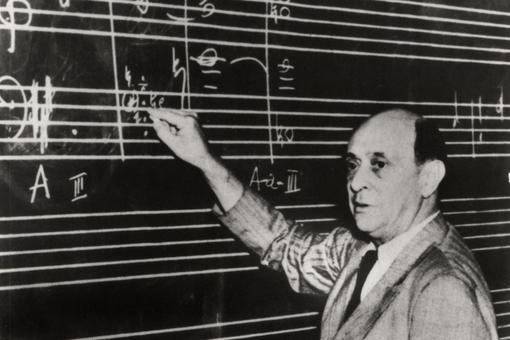 Schwarzweiß-Foto von Arnold Schönberg unterrichtend, der auf eine schwarze Tafel Noten schreibt