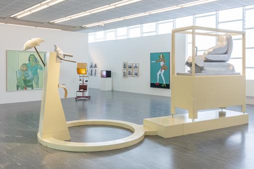 Ausstellungsansicht: Gemälde auf weißem Hintergrund, im Vordergrund eine Skulpturengruppe