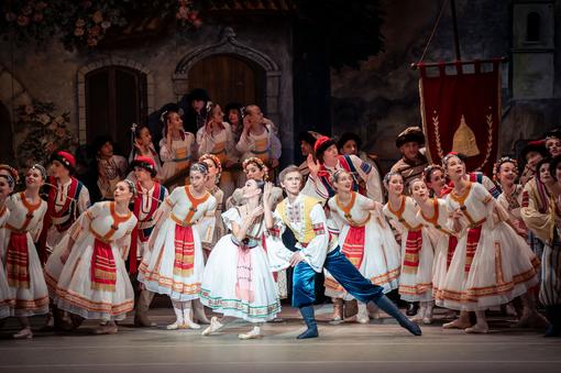 Foto zahlreicher Tänzer:innen in volkstümlichen Kostümen in Weiß und Rot, im Vordergrund das Solistenpaar