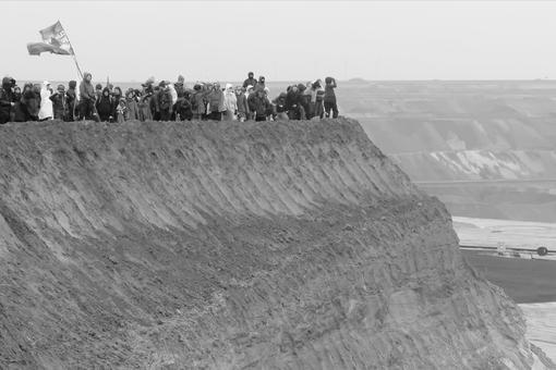 Das Schwarzweiß-Foto zeigt eine Protestkundgebung von Menschen an einem steilen Abruch im Kohle-Tagebau-Gebiet von Lützerath