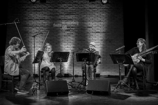 Black and white photo of a Schrammelquarett consisting of two women and two men making music with their instruments: two violins, one button harmonica and one contraguitar