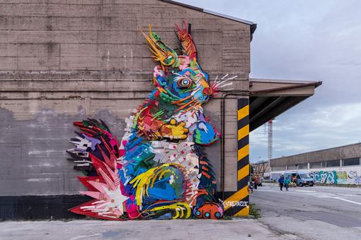 Photo of street art mural, motive: colorful squirrel, in front of it four people holding hands