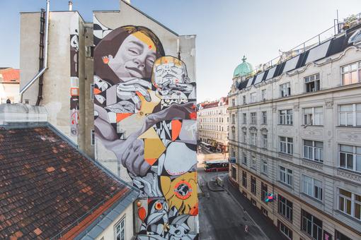 Foto einer bunten Street-Art Wand, die eine Frau mit Baby im Arm zeigt, gegenüber einer Häuserfront 