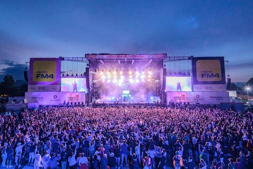 The photo shows an act on the main stage of the Donausinselfest in the evening, with a large audience in front of the stage