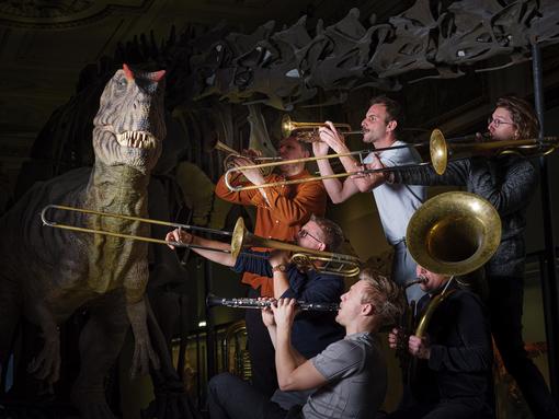 Musicians with wind instruments next to the Allosaurus model in the Natural History Museum Vienna