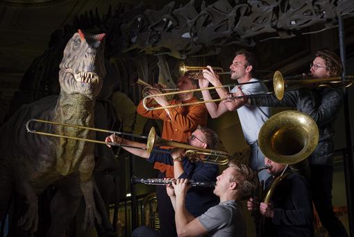 Musicians with wind instruments next to the Allosaurus model in the Natural History Museum Vienna