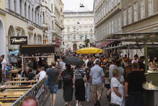 The photo shows an alley in Vienna with numerous visitors to the Freihausviertel Festival, stalls, small guest gardens, etc.