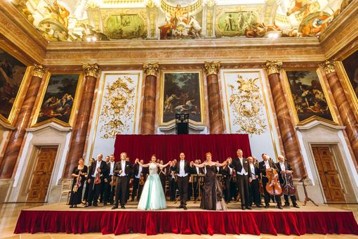 The photo shows the Vienna Hofburg Orchestra with female vocal soloists in long evening gowns in the Herkulessaal of the Liechtenstein Garden Palace