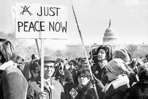 Black and white photo of a demonstration for peace in front of the Capitol in Washington, in the foreground a man carrying a placard with the words "Just Peace Now"
