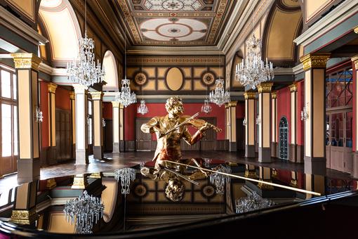 Foto des Strauss-Saales im Casino Zögernitz, im Vordergrund eine goldenen Strauss-Statue, die an einem schwarzen Konzertflügel steht