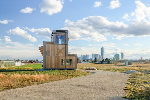 Modern building made of wood on a field, in the background the skyline of Vienna