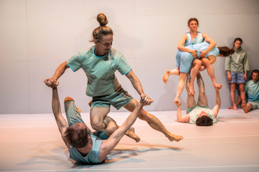 Das Foto zeigt eine Tanzperformance mit 5 Protagonist:innen in pastellfarbenen Trikots. Es sieht so aus, als würden die Tänzer:innen miteinander ringen.
