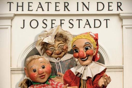 Photo of three figures from the Punch and Judy show: Punch, a boy and the grandmother, with the words "Theater in der Josefstadt" above them.