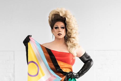 Photo of drag queen Ryta Tale with the flag of LGBTQIA+ as a cape