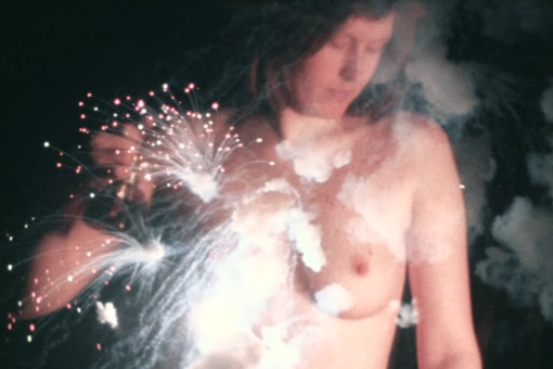 The photo shows the upper body of a naked woman holding a perfume bottle in her hand, in the foreground sparks as if from a spray candle