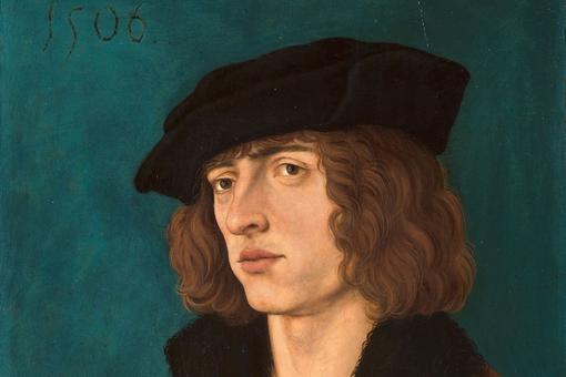 Portrait of a young man with brown, chin-length, curly hair and a black hat