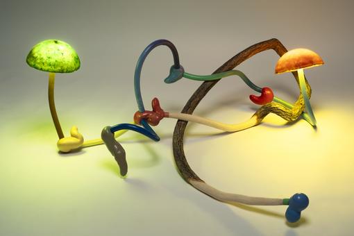 The photo shows an object consisting of a bent branch with some of the bark removed, connected to curved blue and green plactic cables and two small lamps that look like mushrooms.