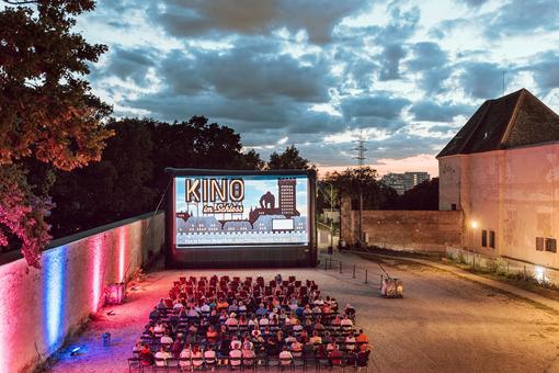 Das Foto zeigt das Open-Air-Kino "Kino im Schloss" im Schloss Neugebäude in abendlicher Stimmung, zu sehen ist eine Leinwand, davor Stuhlreihen mit dem Publikum