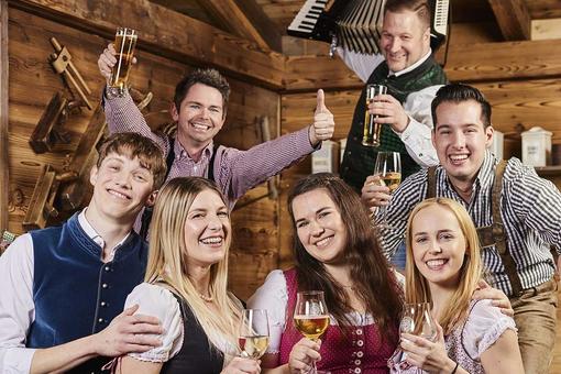 Foto mit vier jungen Männern und drei jungen Frauen in Tracht in Partystimmung mit einem Glas Wien oder Bier in der Hand