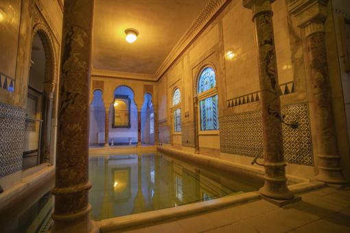 The photo shows an oriental-style interior with columns, mosaic tiles and a swimming pool in the middle of the room