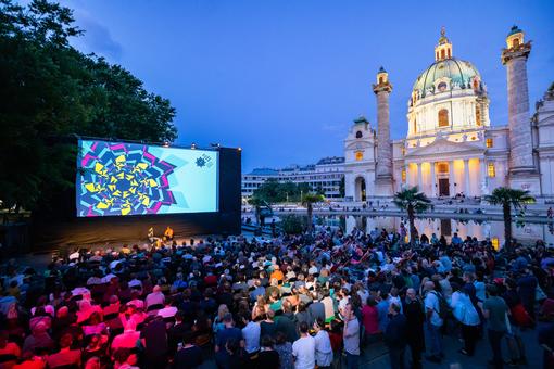 Photo from the Kaleidosp film festival: in the foreground the screen and the audience, in the background the baroque Karlskirche church.