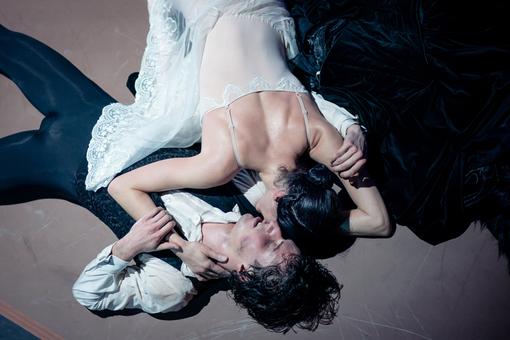 The photo shows the soloist couple from the ballet The Lady of the Camellias lying on the floor in white and black costumes, hugging each other with an exhausted but strong expression on their faces 