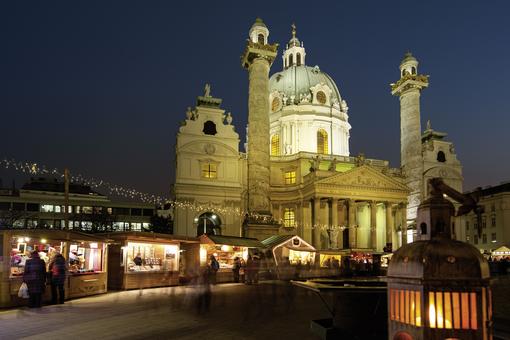 Photo of the illuminated baroque Karlskirche at night, in front of it illuminated and decorated stalls of the Advent market.