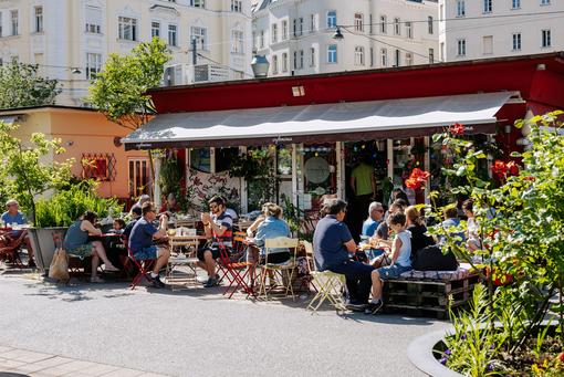 Foto einer Markszene am Karmelitermarkt mit einem belebten Gastgarten
