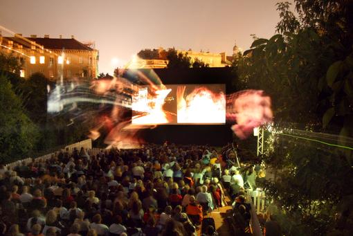 Photo shows the open-air cinema in the garden of the Austrian Film Archive, view of the screen, in front of it the audience 