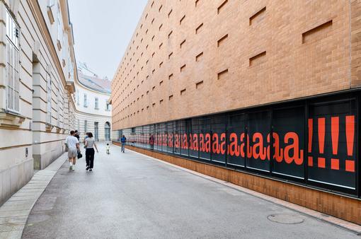 Zu sehen ist Nora Turatos 62 Meter langes Wandbild an der südwestlichen Außenwand der Kunsthalle Wien, dies besteht aus unzähligen roten Buchstaben a und am Ende mit Rufzeichen auf dunklem Hintergrund