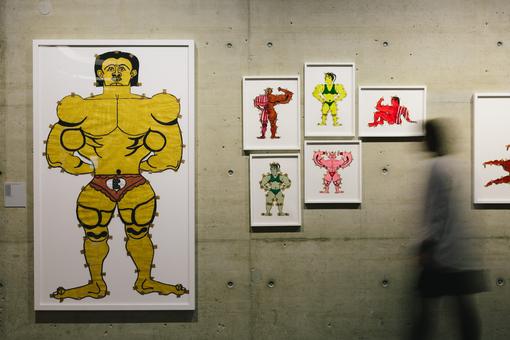Ausstellungsansicht: ein großes und fünf kleinere Bilder mit Zeichnungen von männlichen und weiblichen Bodybildern in unterschiedlichen Farben