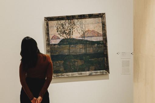 Das Foto zeigt eine Besucherin, die ein Gemälde von Egon Schiele betrachtet. Das Gemälde ist absichtlich schief gehängt.