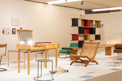 Aussstellungsansicht mit unterschiedlichen Design-Möbelstücken vorwiegend aus Holz, ein Regal, ein Kosmetiktisch, unterschiedliche Stühle und Hocker