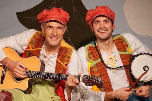 Two musicians in costume and with orange caps, one holding a guitar, the other a drum