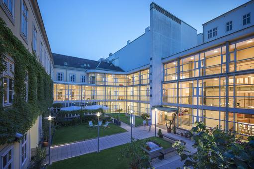 The photo shows the greened and illuminated inner courtyard and glass façade of the Vienna Furniture Museum in the evening