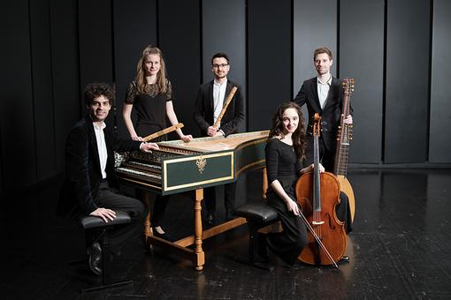 The photo shows the MokkaBarock ensemble for baroque music, two women and three men in black and white clothing, with baroque musical instruments, grouped around a harpsichord