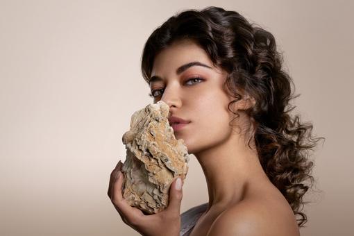 Porträtfoto einer jungen Frau mit langem welligem braunem Haar, die der Vorstellung der Carmen entspricht. Sie hält einen Stein in Händen