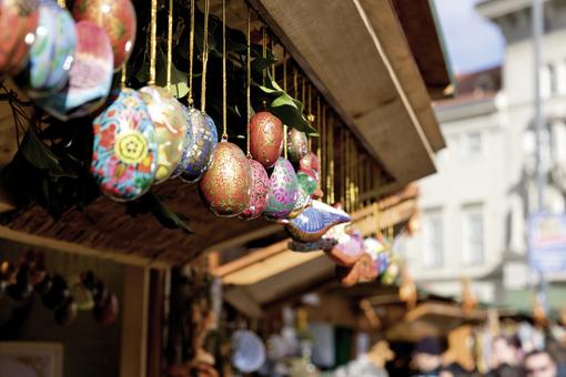 Foto von bunt verzierten Ostereiern, die mit goldenen Fäden hintereinander bei einem Marktstand aufgehängt sind