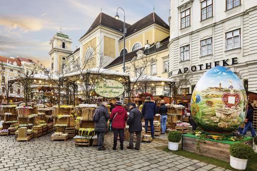 Scene at the Old Viennese Easter market with stalls, boxes with painted Easter eggs, in the foreground an oversized painted egg, in the background a church