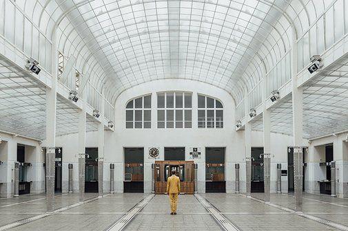 The photo shows the large cash hall of the Postsparkasse, which was designed by Otto Wagner. A man in a yellow suit stands in the middle of the hall with his back to the camera