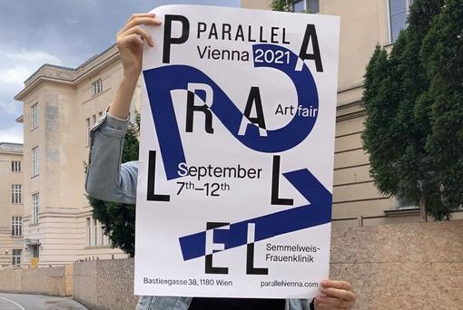 The poster of Parallel Vienna is held up to the camera, with the Semmelweis Women's Clinic in the background.